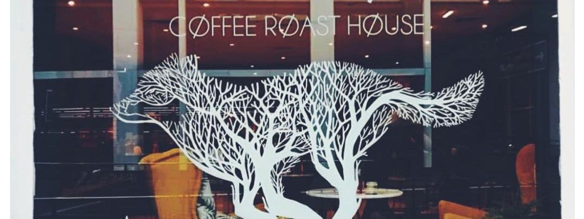 A decorative window display at Wolfox Coffee featuring a stylized white silhouette of a wolf intertwined with tree branches. The words "Coffee Roast House" are visible above the design, creating a welcoming atmosphere for visitors.