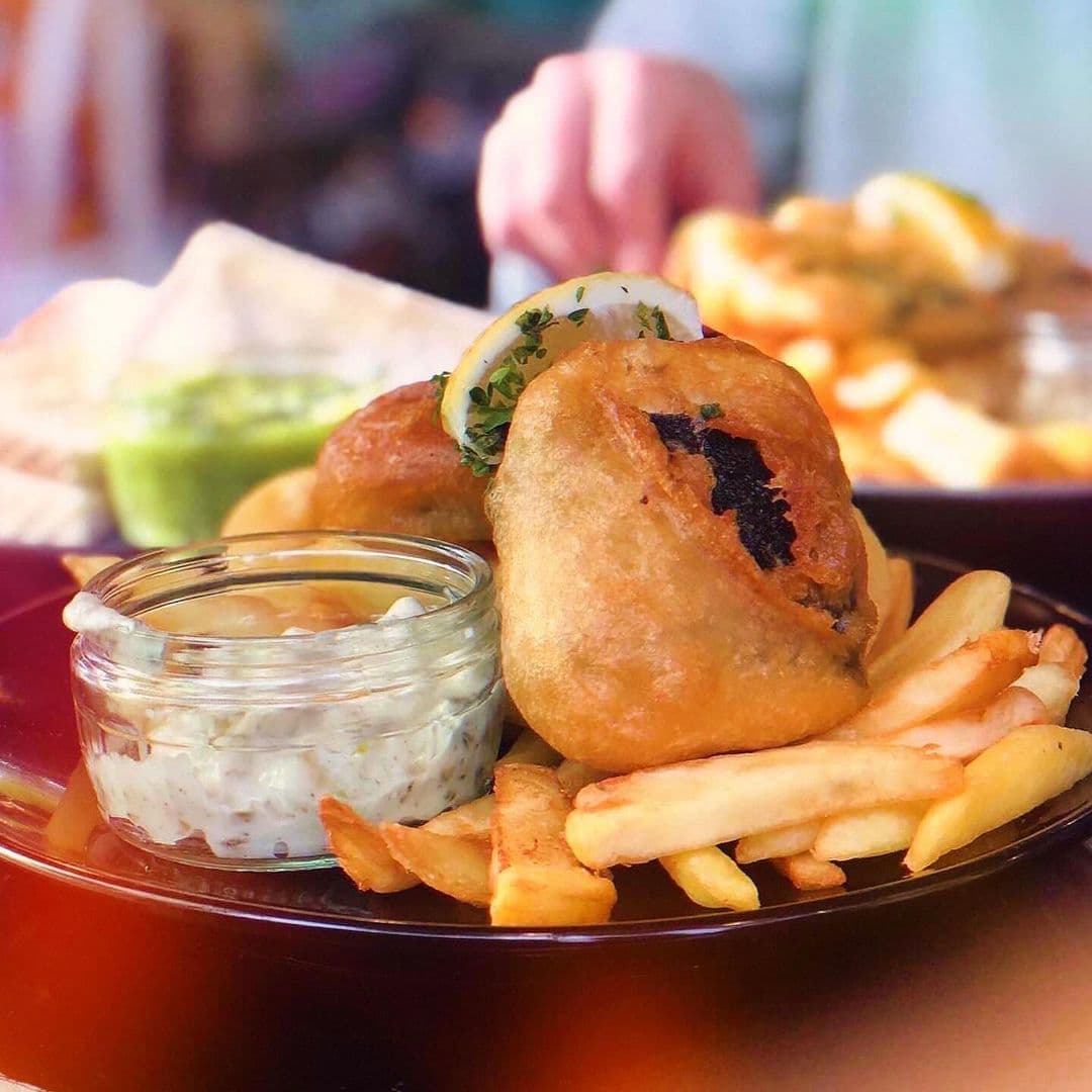 Scoffs Feel Good Food delicious snack fried food fries dipping sauce Delicious plate of food from Scoffs Feel Good Food featuring crispy fried items, golden French fries, and a small jar of dipping sauce. A slice of lemon and fresh herbs garnish the fried items, adding a pop of color.