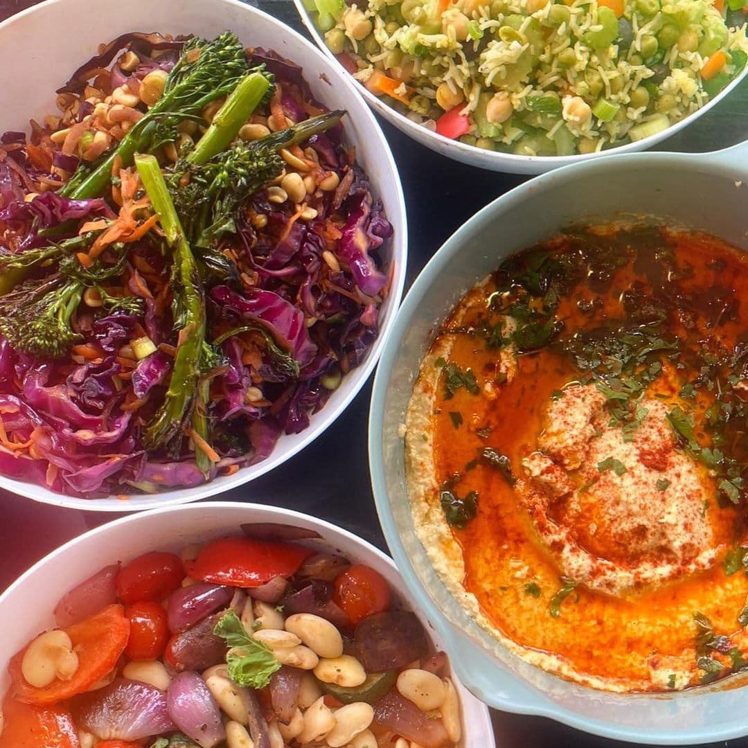Scoffs Feel Good Food healthy vegan dishes fresh salads hummus A colorful assortment of healthy dishes from Scoffs Feel Good Food. The image features a bowl of vibrant purple cabbage salad topped with pine nuts, a creamy hummus drizzled with olive oil and spices, a fresh vegetable medley with tomatoes and beans, and a light rice salad with mixed vegetables.