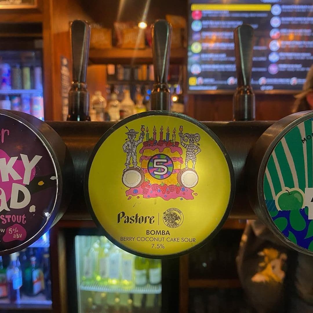 The Head of Steam Park Row craft beer tap brewery pub unique Alt text: A close-up of beer taps at The Head of Steam – Park Row, featuring a colorful label for "Bomba" Berry Coconut Cake Sour by Pastore, with a birthday cake design and vibrant colors.