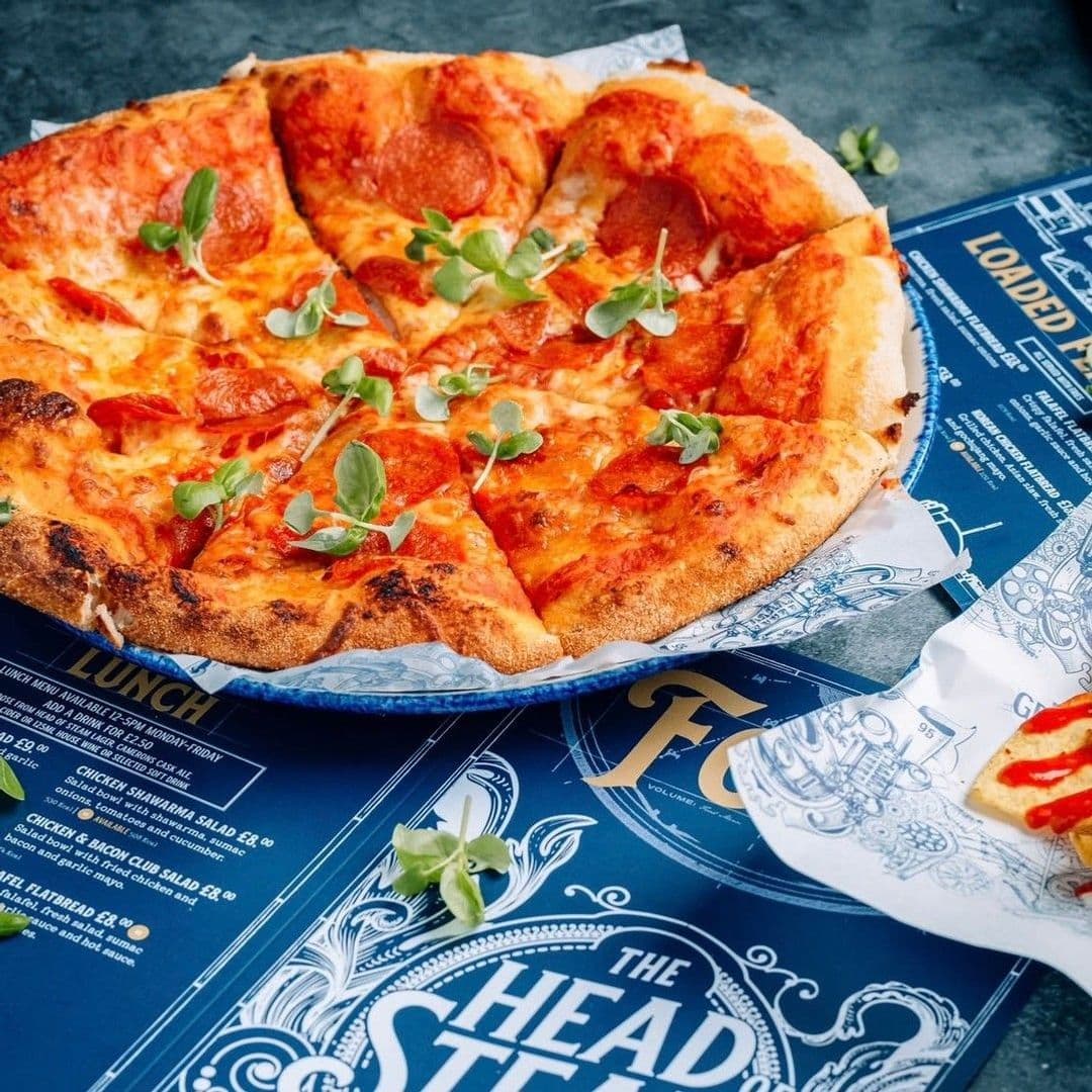 The Head of Steam Park Row delicious pizza dining experience restaurant Delicious pepperoni pizza garnished with fresh greens, served on a blue menu at The Head of Steam – Park Row.