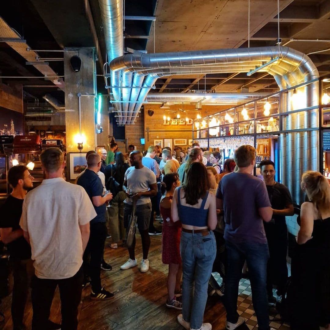 The Head of Steam Park Row lively crowd socializing bar interior A lively crowd enjoying drinks and conversation inside The Head of Steam – Park Row. The bar features industrial decor with exposed pipes and warm lighting, creating a welcoming atmosphere for socializing.