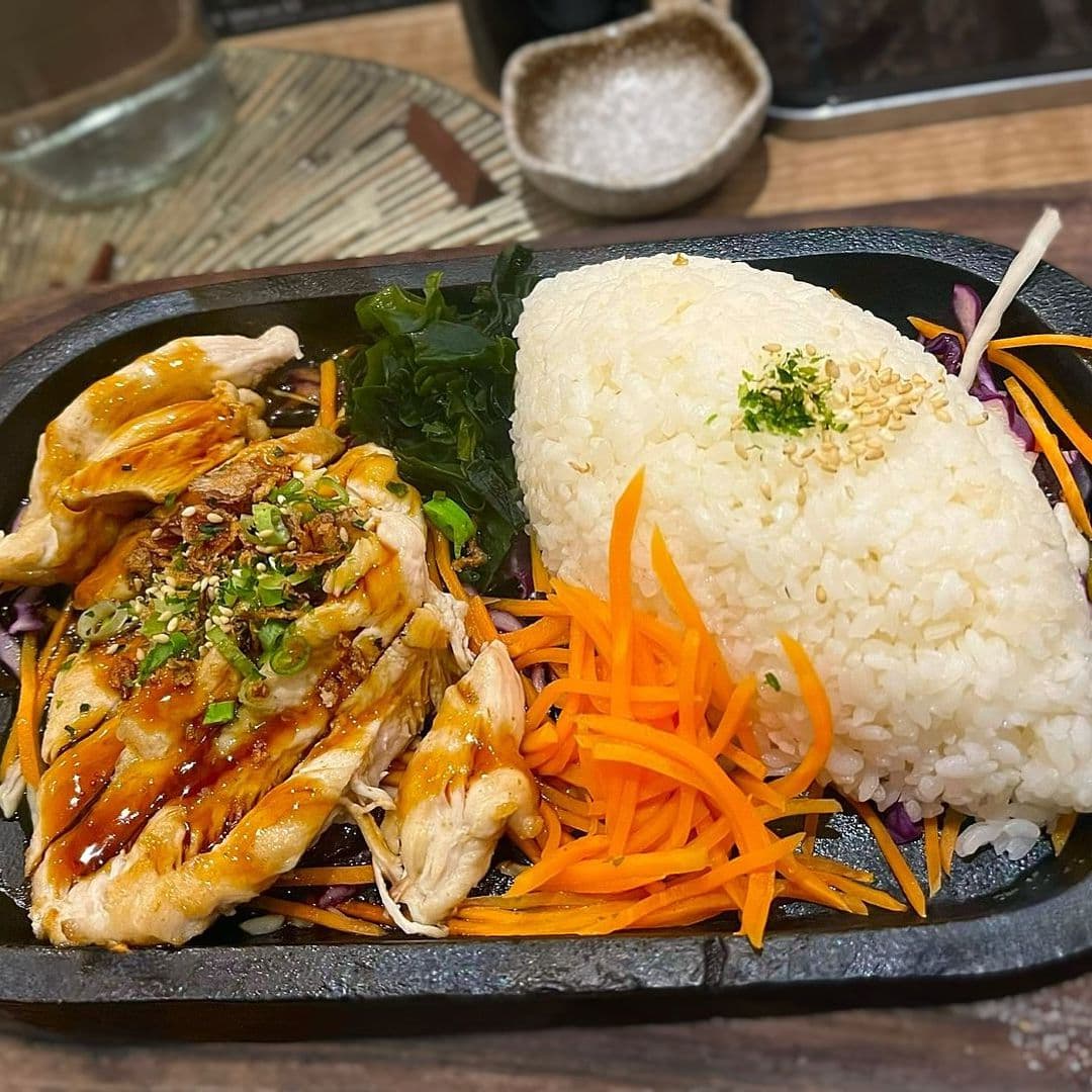 Fern Modern Sushi grilled chicken rice vegetables sushi dish Delicious grilled chicken served on a hot plate with colorful vegetables, including carrots and seaweed, alongside a mound of fluffy white rice. This dish is featured at Fern Modern Sushi.