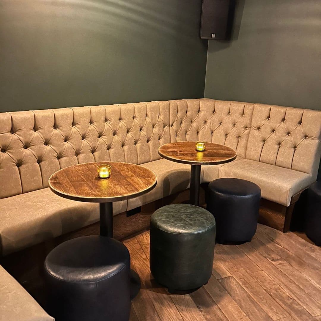 Adel Tap cozy interior lounge seating tables warm lighting Cozy seating area at Adel Tap featuring plush, tufted benches and wooden tables. Soft lighting creates a warm atmosphere, making it an inviting spot for relaxation and socializing.