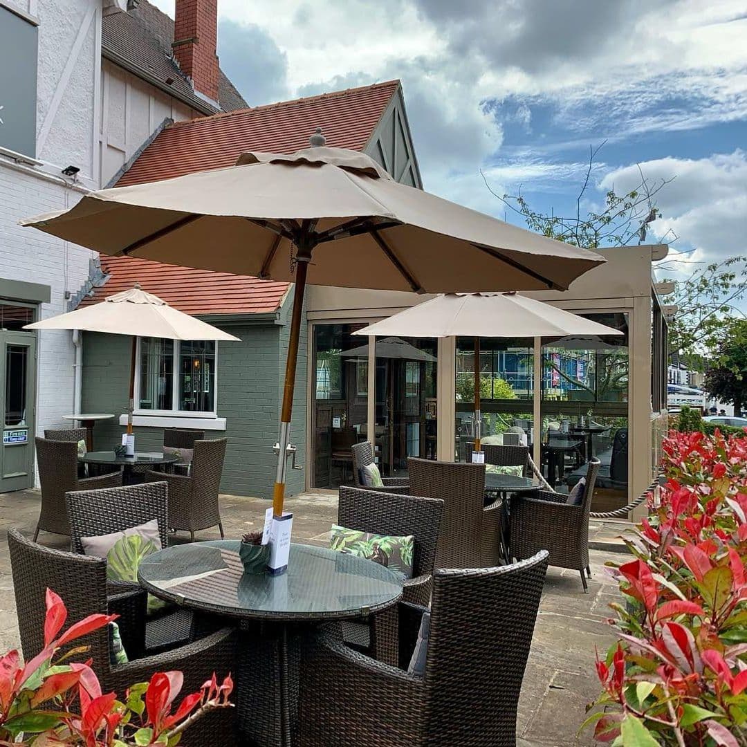 Deer Park Hotel outdoor dining relaxing scenery sunny day Outdoor seating area at Deer Park Hotel featuring wicker tables and chairs under large umbrellas, surrounded by vibrant plants and a view of the hotel building.