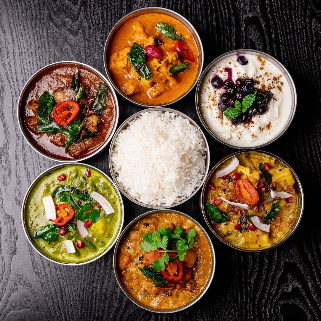 Kerala canteen authentic dishes indian cuisine rice thali A vibrant spread of traditional dishes from Kerala canteen, featuring a variety of curries in metal bowls, alongside a serving of fluffy white rice. The dishes include colorful ingredients like green vegetables, spices, and garnishes, showcasing the rich flavors of Kerala cuisine.