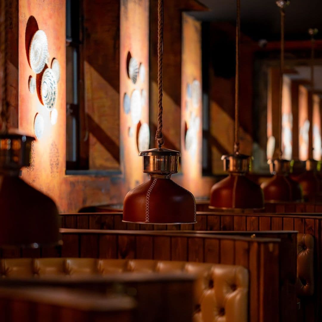 Kerala canteen cozy interior restaurant lighting ambiance Alt text: Interior view of Kerala canteen, featuring warm lighting from stylish hanging lamps and cozy wooden booths. The walls are adorned with decorative plates, creating a welcoming atmosphere for diners.