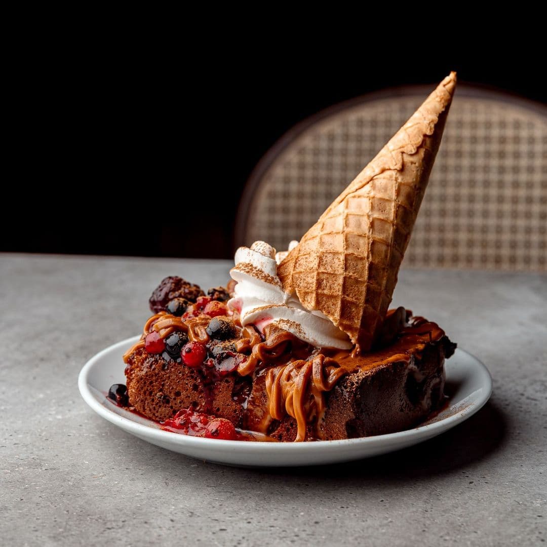 Nesso Coffee dessert chocolate berries ice cream Delicious dessert served at Nesso Coffee, featuring a slice of chocolate cake topped with caramel sauce, fresh berries, whipped cream, and a waffle cone.