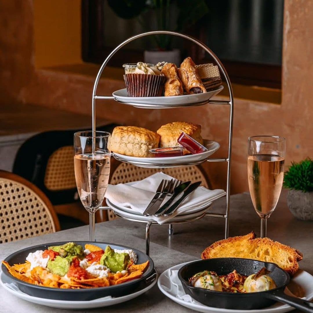 Nesso Coffee gourmet food afternoon tea dining experience A beautifully arranged table at Nesso Coffee featuring an elegant tiered stand with pastries, a cupcake, and scones with jam. In front, a plate of nachos topped with guacamole and cheese, alongside a small skillet dish. Two glasses of sparkling drink complete the inviting setup.