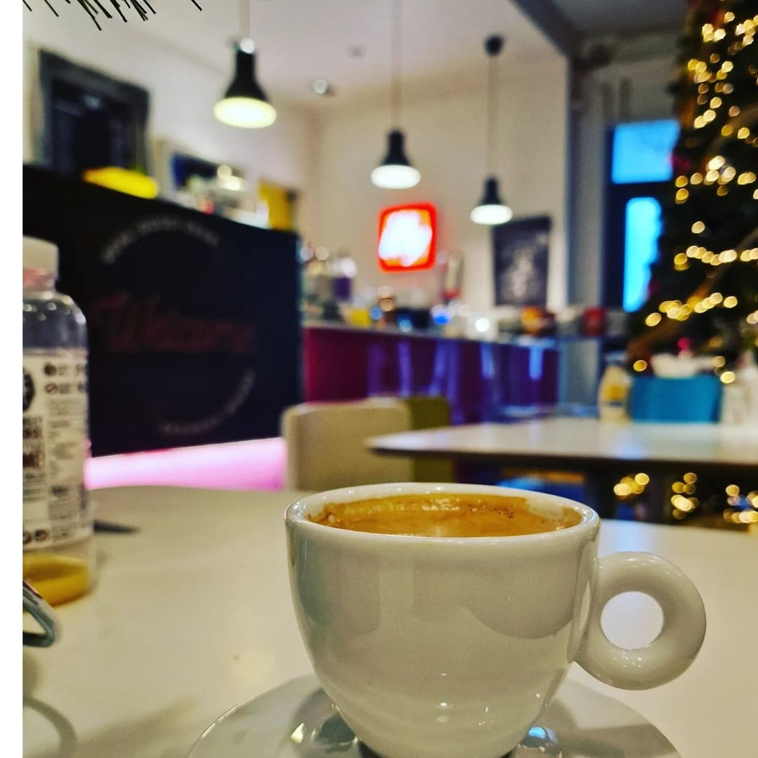 Cozy Espresso Experience with Holiday Ambiance A close-up of a white coffee cup on a table, with a festive Christmas tree and cozy cafe ambiance in the background.