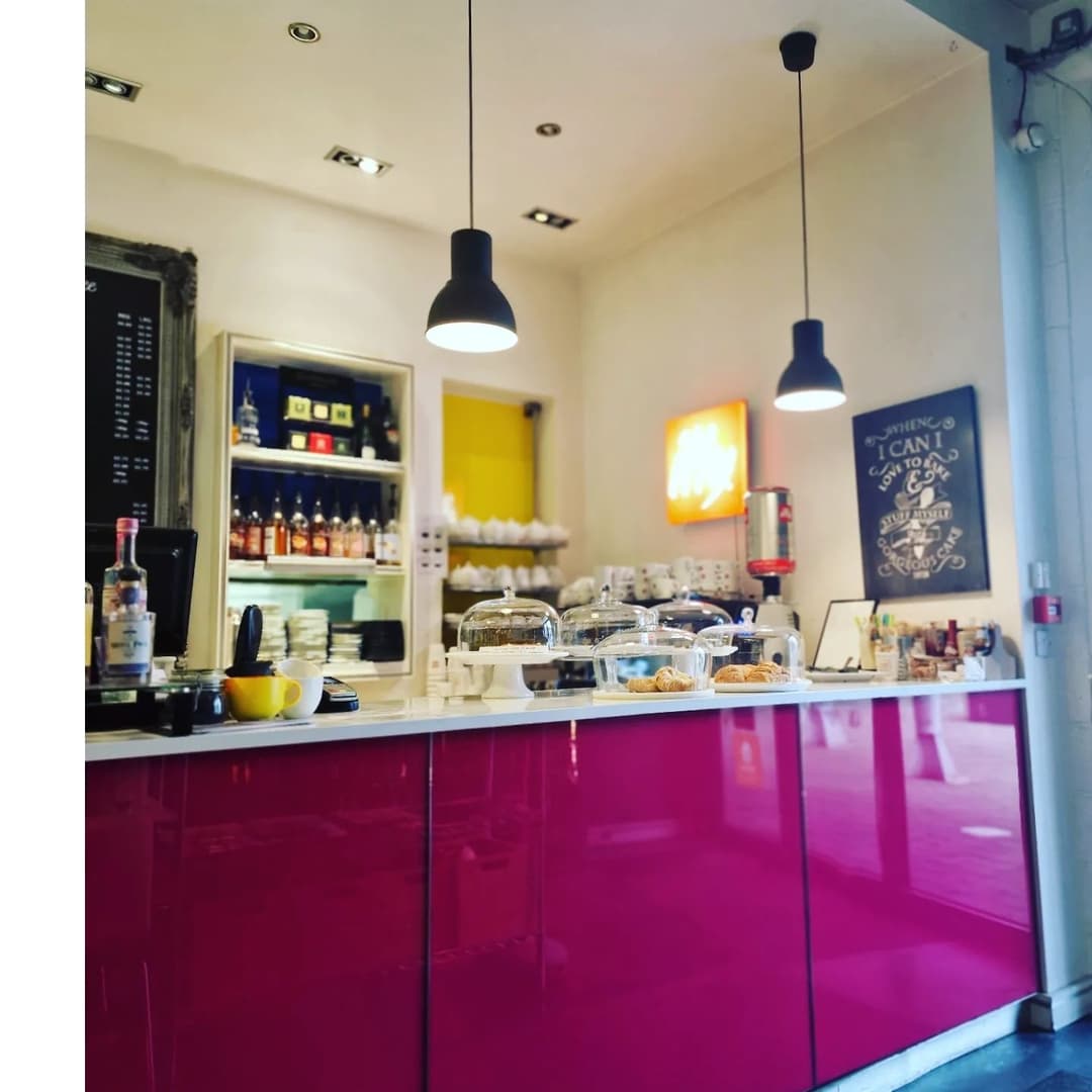 Vibrant Counter with Artisan Pastries Bright café interior with a vibrant pink counter, glass display of pastries, and stylish pendant lights overhead.