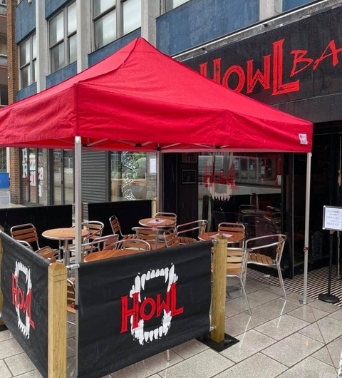 Inviting Outdoor Patio with Red Canopy Red canopy over outdoor seating with wooden tables and chairs, creating a vibrant, inviting atmosphere at Howl Bar Leeds.