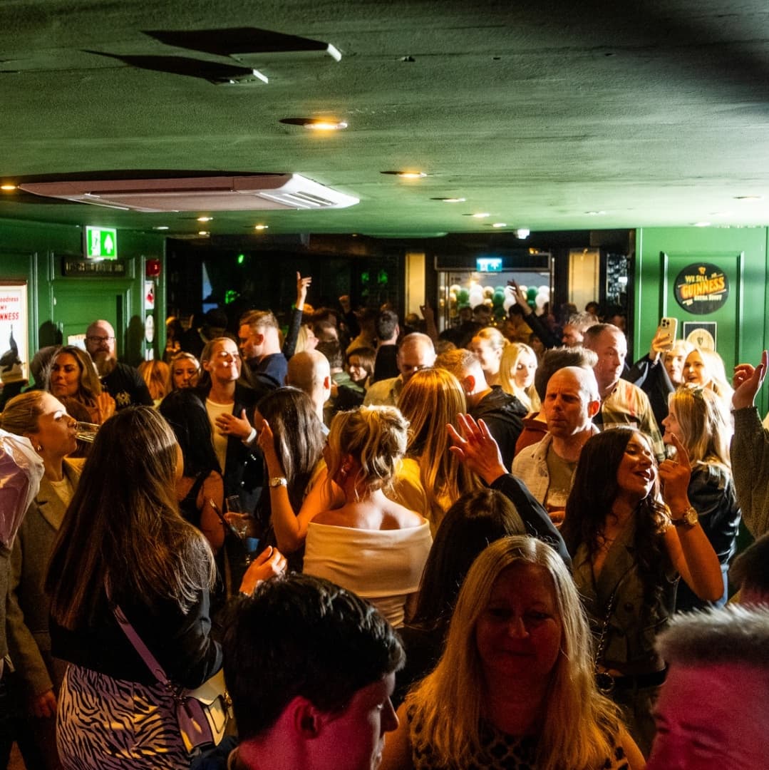 Vibrant Nightlife Scene at Katie O’Brien’s Crowded tavern scene with lively patrons enjoying drinks, vibrant atmosphere, and green decor enhancing the Irish theme.