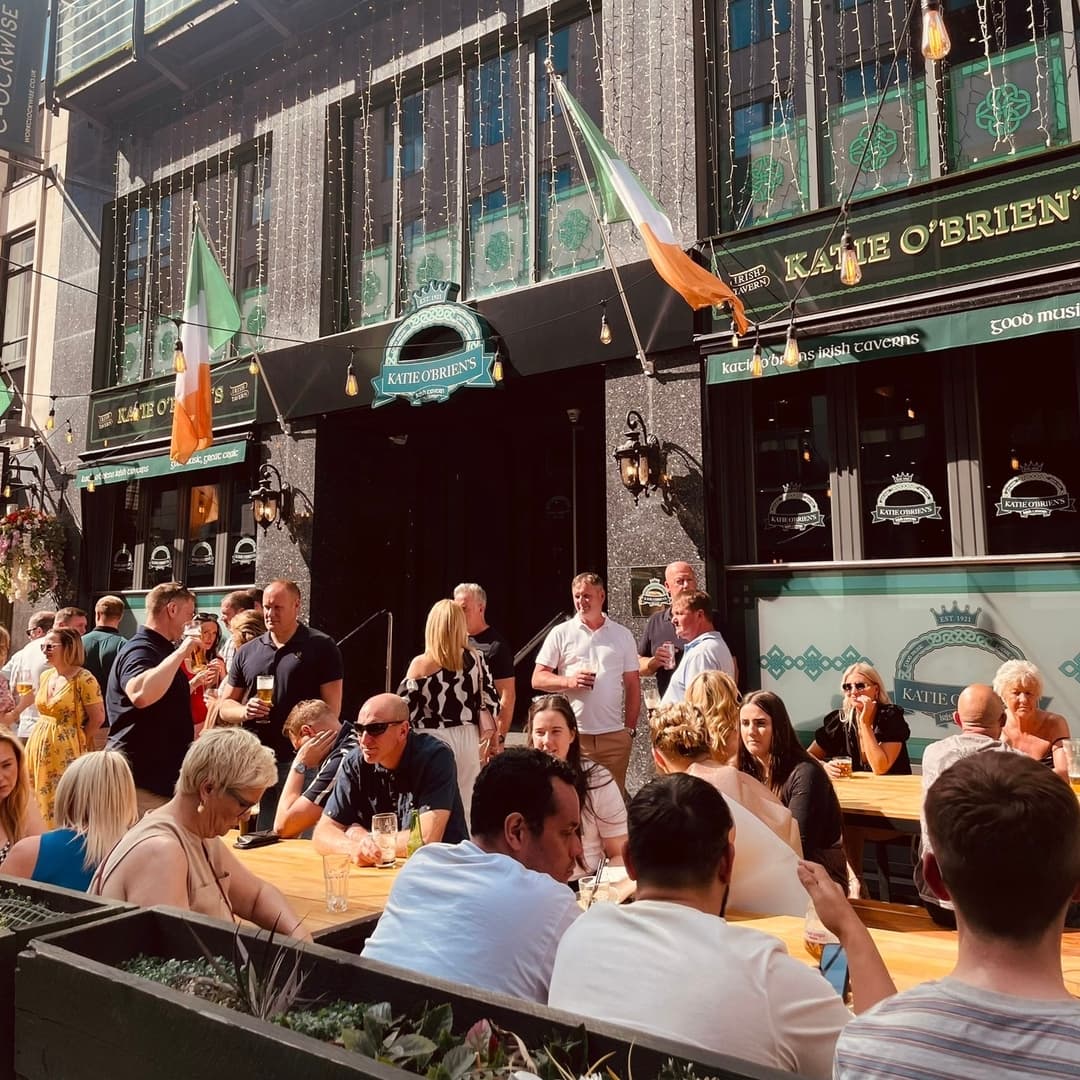 Vibrant Outdoor Seating at Katie O’Brien’s Lively outdoor seating at Katie O'Brien's Irish Tavern, with patrons enjoying drinks and Irish flags adorning the facade.