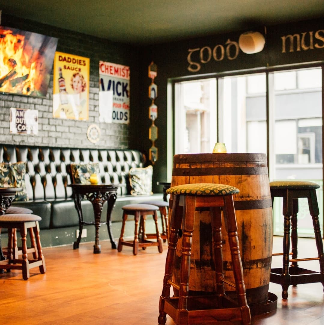 Cozy Seating with Vintage Decor Cozy tavern interior with wooden stools, a barrel table, and green walls adorned with vintage posters and warm lighting.
