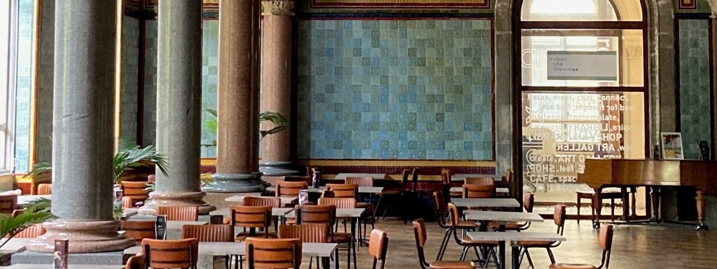 Elegant Tiled Hall Café features tall columns, wooden tables, and a grand piano, creating a warm, inviting atmosphere.