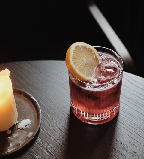 The Penny Bun — card The Penny Bun — deep red cocktail with citrus garnish and candle