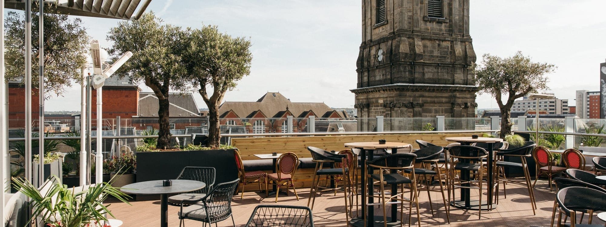 CrowdedHouse rooftop terrace with bistro tables, olive trees and Leeds city church tower