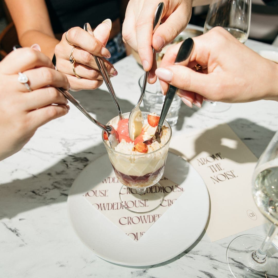 crowdedhouse-gallery-06 Hands sharing a strawberry sundae dessert on a CrowdedHouse branded marble table