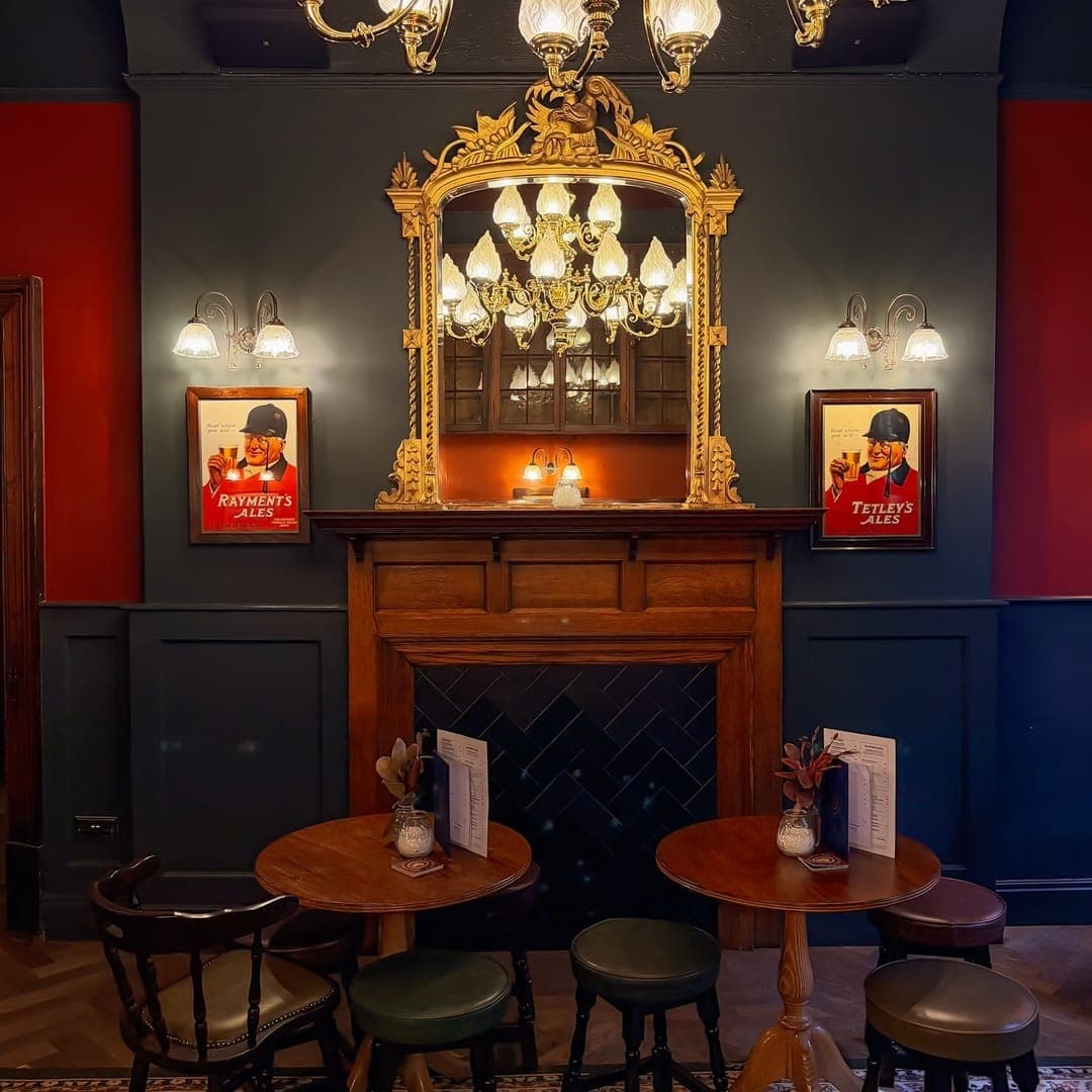 the-victoria-and-commercial-pub-fireplace-chandelier Victorian fireplace with ornate gold mirror and brass chandelier at The Victoria and Commercial pub with vintage Tetleys posters