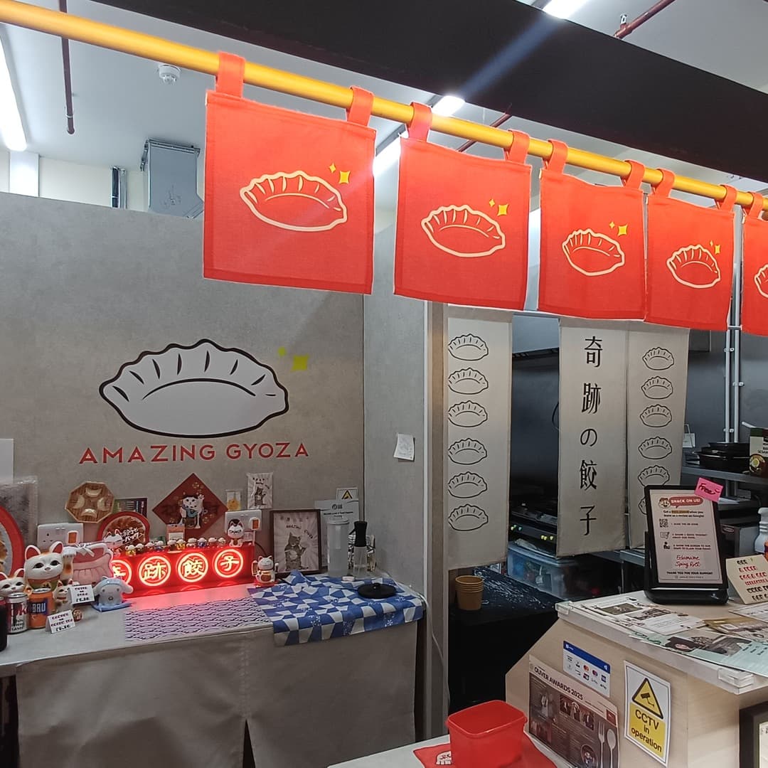 Amazing Gyoza — wall logo and red dumpling banners The Amazing Gyoza wall logo with red dumpling-print banner curtains, Japanese signage, lucky cats and a red neon sign at the stall in Kirkgate Market, Leeds.