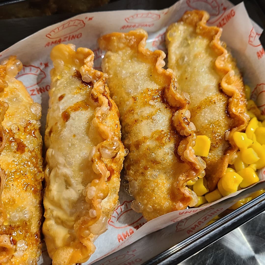 Amazing Gyoza — close-up of fried gyoza A close-up of four crisp fried gyoza on branded Amazing Gyoza paper with sweetcorn at the side.