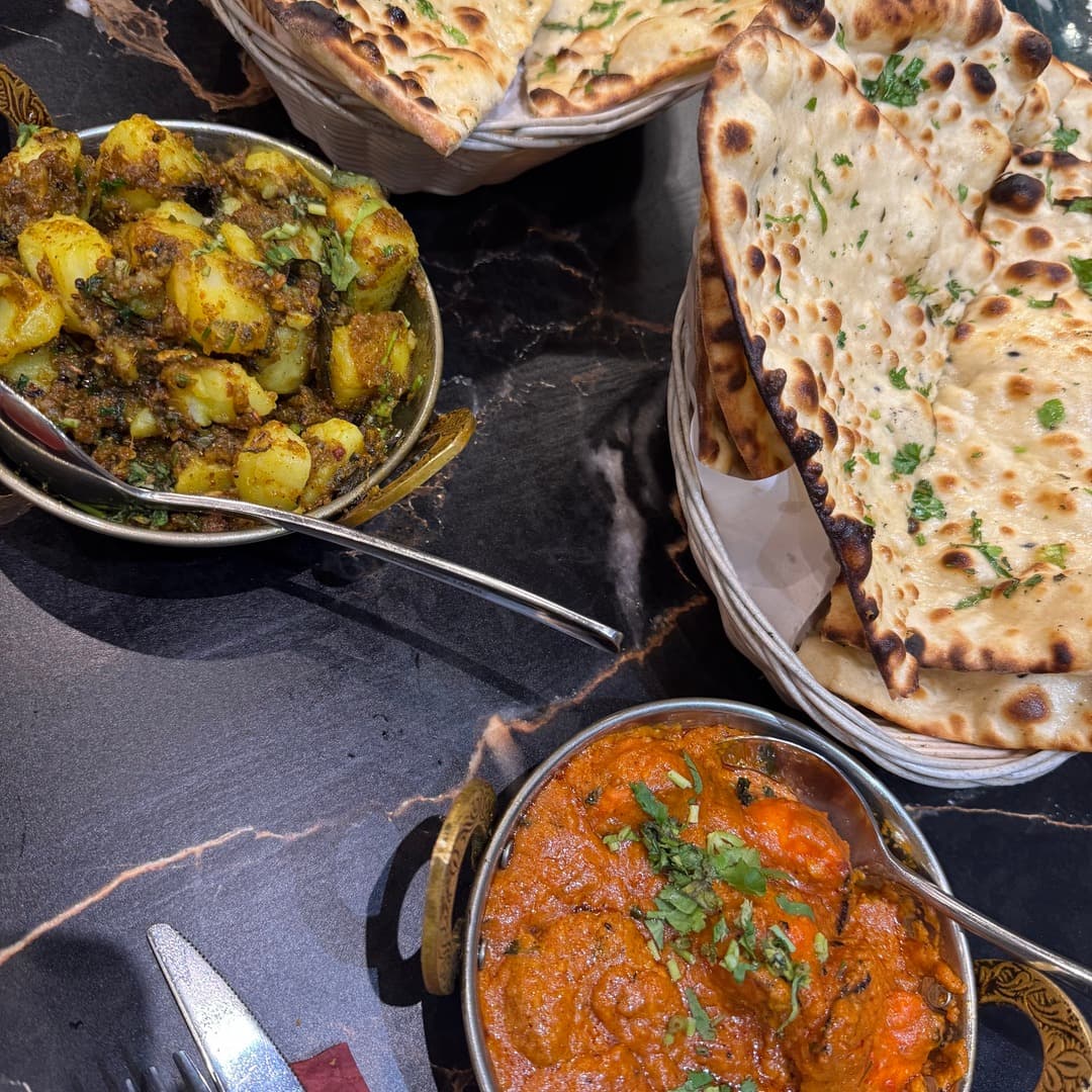 Bombay Junction — naan with aloo and chicken curry Two baskets of naan, a copper bowl of aloo curry with potatoes and a copper bowl of chicken curry, on a black marble table at Bombay Junction, Leeds.