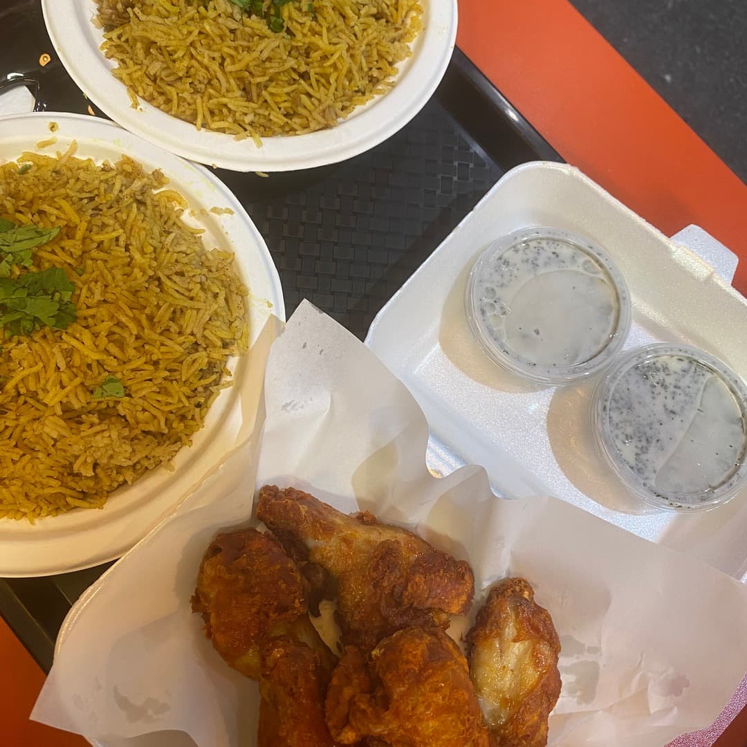 Leziza — biryani with fried chicken and raita Two bowls of biryani with a basket of fried chicken pieces and two raita dips on a tray at Leziza, Leeds Kirkgate Market.