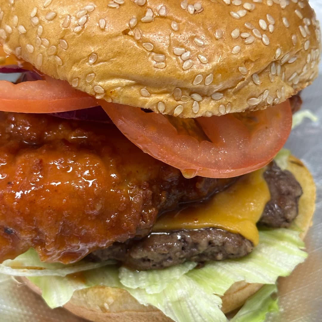Smash Down Leeds — chicken burger with tomato A burger close-up at Smash Down Leeds with battered fried chicken, melted cheddar, tomato slices, lettuce and red onion in a sesame bun.